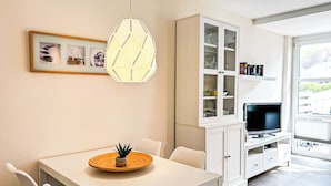 Une cuisine moderne avec une table à manger, des chaises, un meuble avec des portes en verre, un téléviseur et un luminaire suspendu.