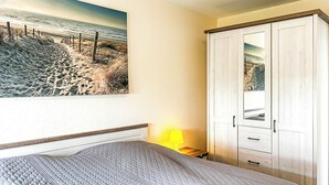 Une chambre à coucher comprenant un lit, une table de chevet, une lampe, une armoire et un tableau sur le thème de la plage accroché au mur.