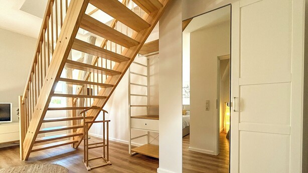 Een ruime kamer met een houten trap, een witte inbouwkast en een deur naar een andere kamer.