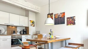 A modern kitchen with white cabinets, a wooden dining table, and a bench. There are hanging lights and artwork on the walls. - Landidyll Wohnung 02 in Elmenhorst (Elmenhorst)