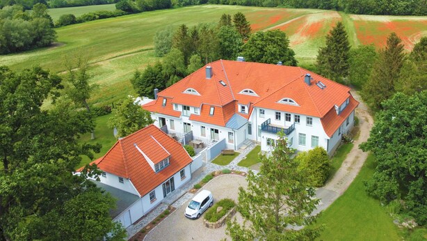 A large, white building with a red roof, surrounded by lush greenery and fields. - Landidyll Wohnung 02 in Elmenhorst (Elmenhorst)
