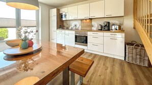 A modern kitchen with white cabinets, a wooden dining table, and a hanging light fixture. - Landidyll Wohnung 03 in Elmenhorst (Elmenhorst)