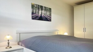 Un dormitorio con cama, mesita de noche, lámpara, armario y un cuadro en la pared.
