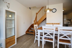 Un coin repas avec un escalier en bois, des chaises blanches et un meuble vitré doté d’étagères.