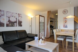 Een moderne woonkamer met een zwarte leren bank, een houten eettafel met stoelen, en een keuken op de achtergrond.