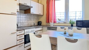 Una cuina moderna amb armaris blancs, un frontó de rajola, una taula de dinar amb caires blanques i una finestra amb cortines vermelles.