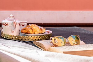 Um livro, óculos de sol, um bule e um croissant numa bandeja.