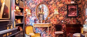 A room with floral wallpaper, a large mirror, a vanity with a lamp, and a chair. - Rosegarden Essence Sintra (Sintra)