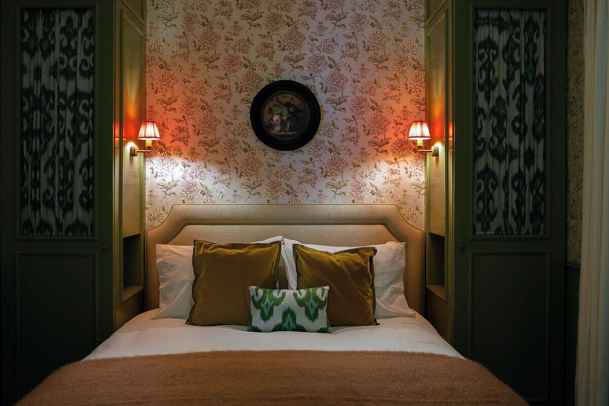 A bedroom with a bed, two wall-mounted lamps, and floral wallpaper.