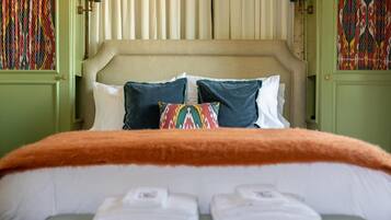 A bed with a beige headboard, white and dark green pillows, and an orange blanket.