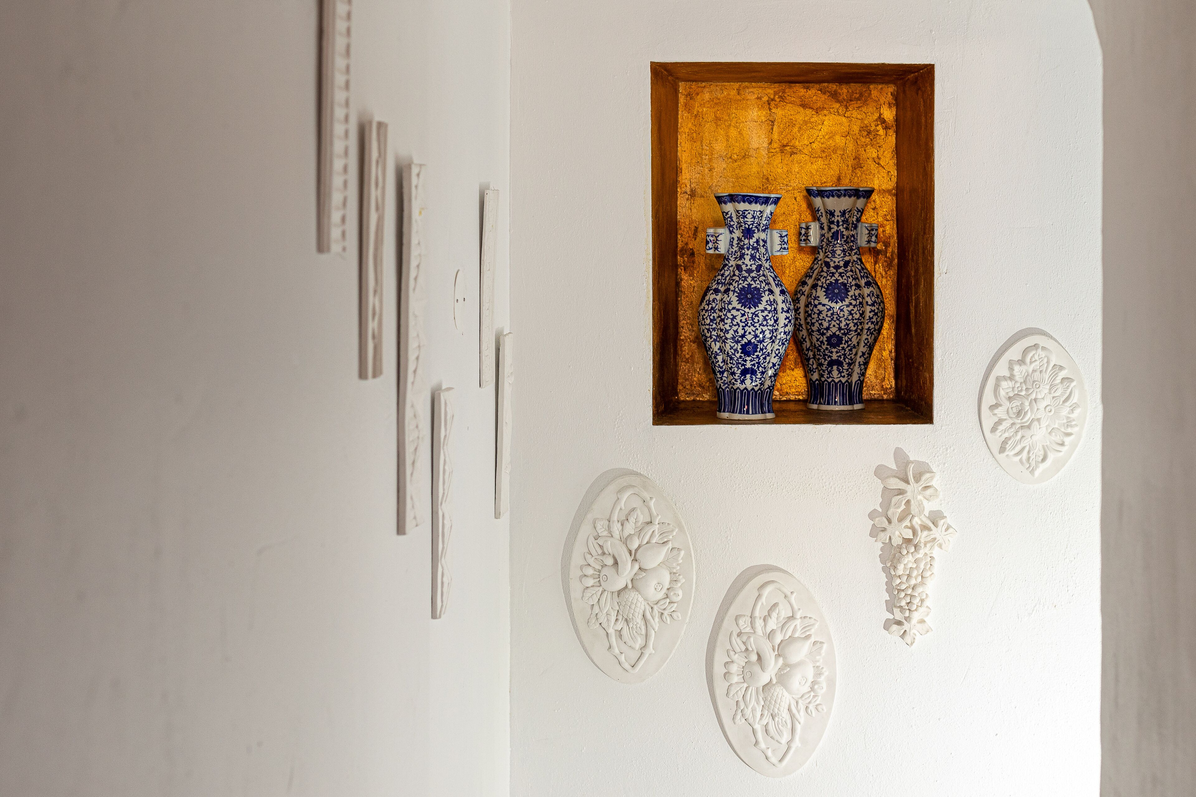 A wall with a framed artwork of two blue and white vases, a wooden door, and decorative wall carvings.