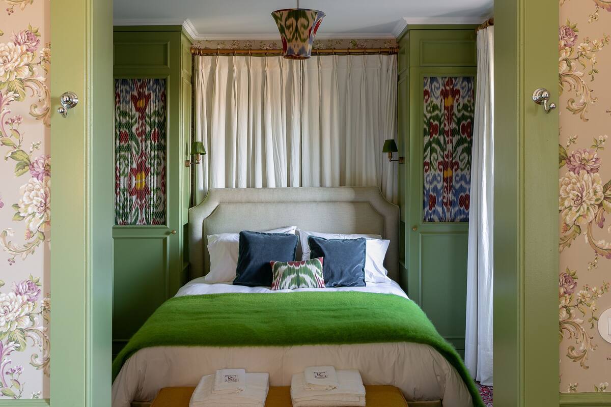 A bed with a green blanket, white bedding, and decorative pillows.