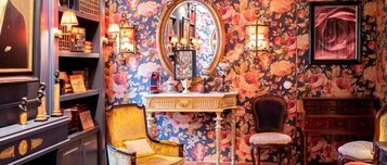 Um quarto com papel de parede floral, um espelho, uma penteadeira com abajur e uma cadeira.