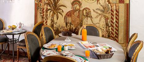 Un comedor con una mesa redonda dispuesta para el desayuno, con platos, pan y una cesta de pasteles.