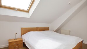 Una camera da letto con finestra sul tetto, una struttura letto in legno, un comodino con cassetti e un termosifone.