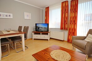 Un salon comprenant une table basse en bois, un téléviseur posé sur un meuble, une table à manger avec des chaises et un canapé.