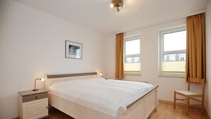 Une chambre avec un lit simple, une table de chevet, une chaise et une fenêtre avec des rideaux.