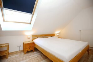 Ein Schlafzimmer mit Dachfenster, einem Holzbett, Nachttischen mit Lampen und einer Holzbank.
