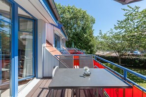 Eine Terrasse mit Tisch und Stühlen, einer Glastür und einem roten Geländer.