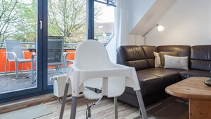 A modern living room with a high ceiling, a leather sofa, a wooden coffee table, and a white chair. - Papillon Wohnung 15-7 (Ostseebad Boltenhagen)