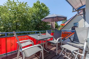 Eine Terrisse im Freien mit Metallstühlen und einem Tisch, einem roten Zaun und einem großen Sonnenschirm.