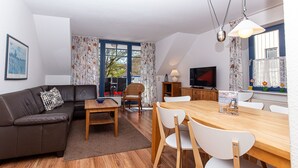 Ein modernes Wohnzimmer mit einer Couch, einem Esstisch mit Stühlen, einem Fernseher und einem Fenster mit Vorhängen.