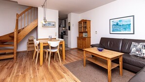 Ein Wohnzimmer mit einer Holztreppe, einem Essbereich mit Tisch und Stühlen, einem braunen Ledersofa und einem gerahmten Bild an der Wand.