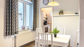 A dining area with a white table and chairs, a potted plant, and a kitchen in the background. - Sünnslag Wohnung 068 (Ostseebad Boltenhagen)