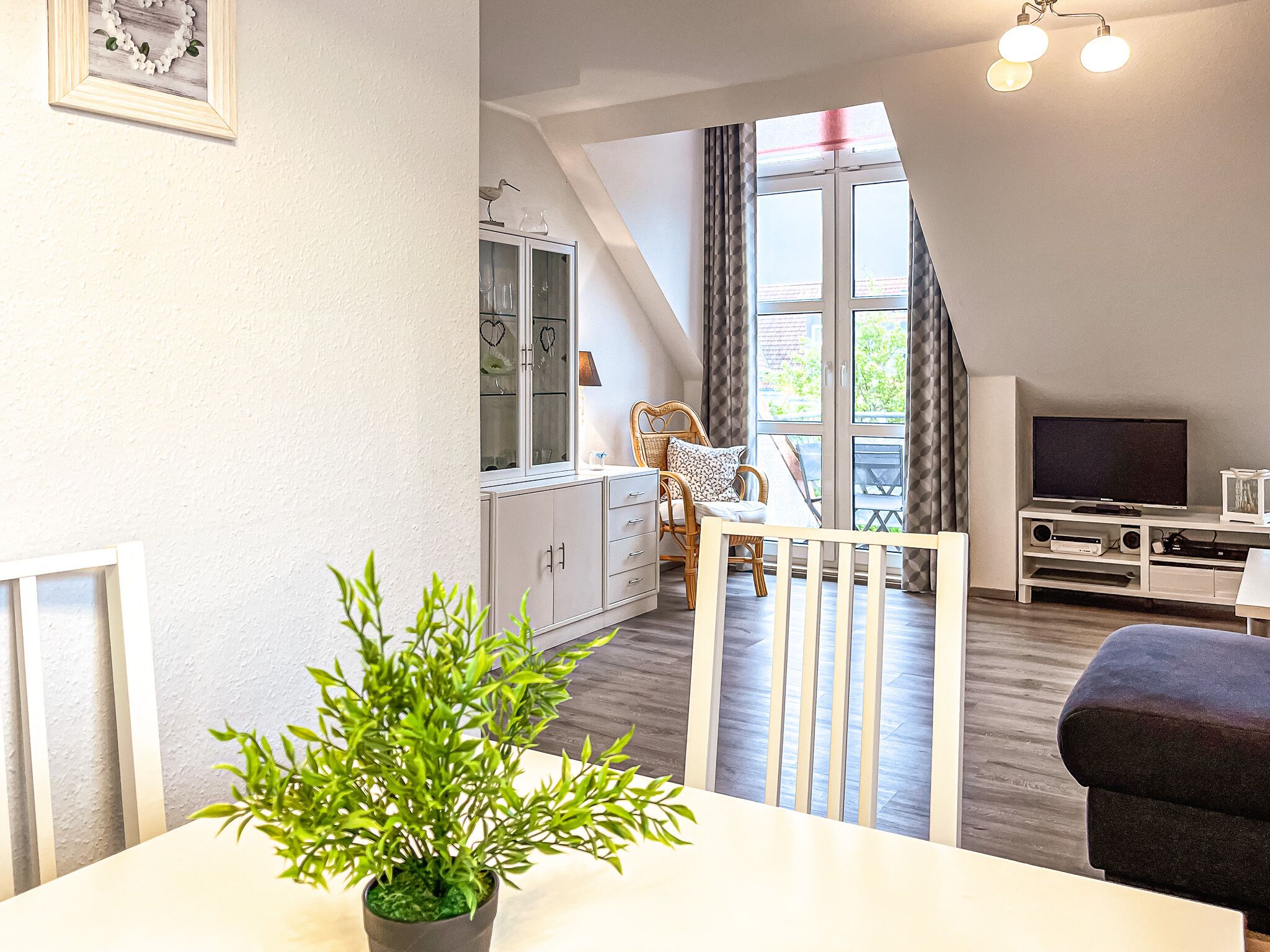 A modern living room with a dining area, a TV, and a balcony with a view.