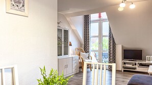 A modern living room with a dining area, a TV, and a balcony with a view. - Sünnslag Wohnung 068 (Ostseebad Boltenhagen)