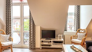 A modern living room with a flat-screen TV, wicker chairs, a coffee table, and a large window offering a view of the outside. - Sünnslag Wohnung 068 (Ostseebad Boltenhagen)