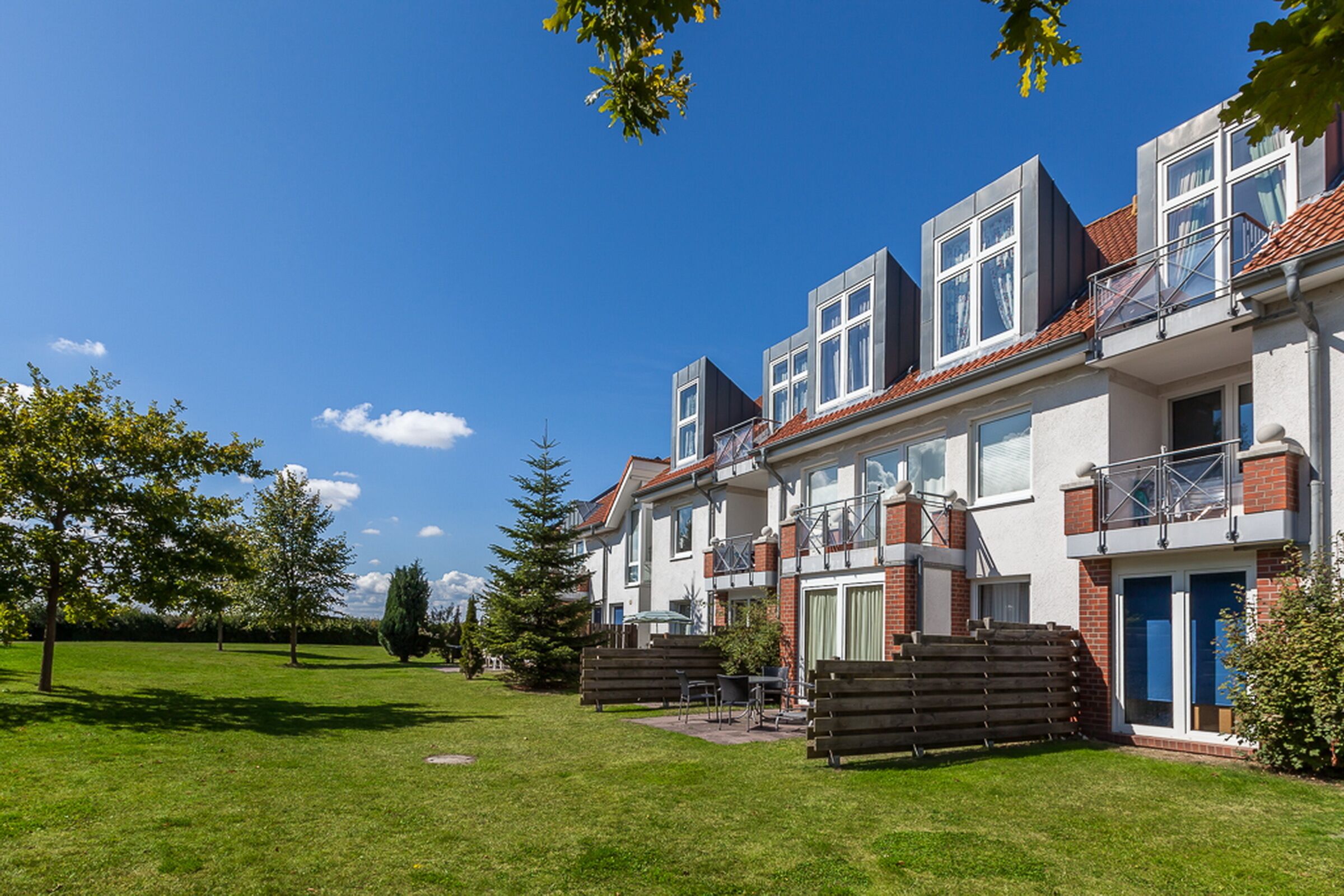 A modern residential building with a well-maintained lawn, outdoor seating area, and a clear blue sky.