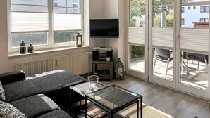 Een woonkamer met een bank, een glazen salontafel, een flatscreen televisie en een radiator.