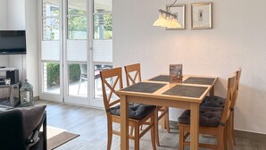 Een eethoek met een houten tafel, vier stoelen, een televisie en een raam met zonwering.