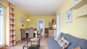 Un salon avec un canapé, un coin repas avec des chaises, une cuisine équipée d’un four à micro-ondes et une porte donnant sur une autre pièce.