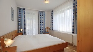 Une chambre à coucher avec un lit en bois, une table de chevet avec une lampe, une chaise et une fenêtre avec des rideaux.