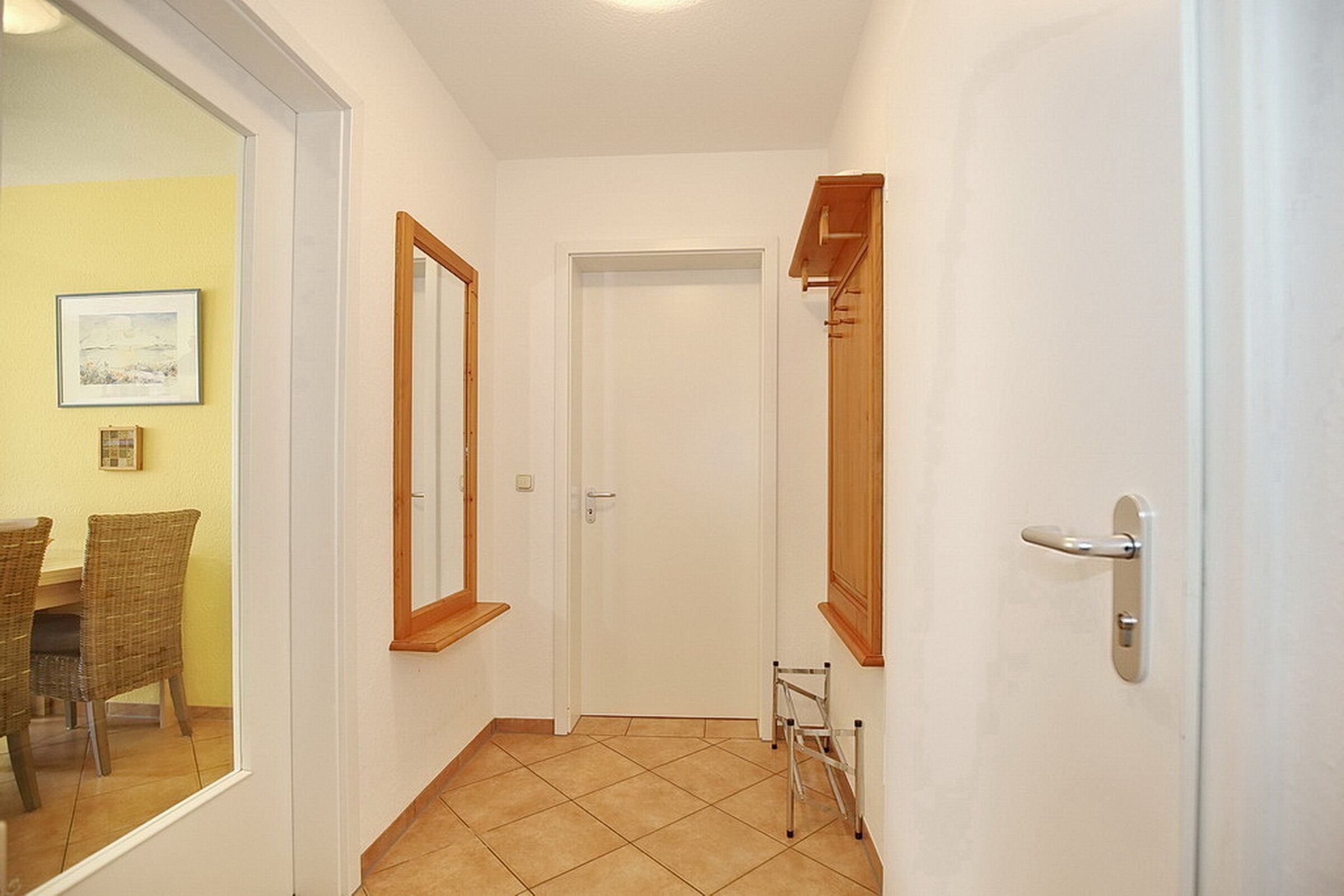 Un pasillo con una puerta blanca, un perchero de madera y una escalera pequeña.