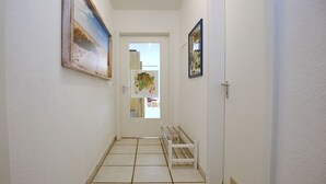 Un pasillo con un banco blanco, una puerta al final y dos cuadros en las paredes.