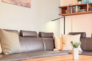 Un sofá de cuero marrón con cojines, un jarrón blanco con una planta y una mesa de centro de madera.