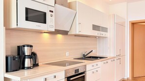 A modern kitchen with white cabinets, a built-in microwave, a coffee maker, and a dishwasher. - Villa Triton Wohnung 03 (Ostseebad Boltenhagen)