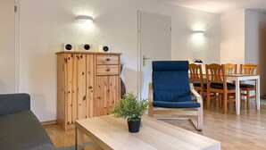 Ein Zimmer mit einem Holzschrank, einem blauen Sessel, einem Esstisch mit Stühlen und einer Topfpflanze.