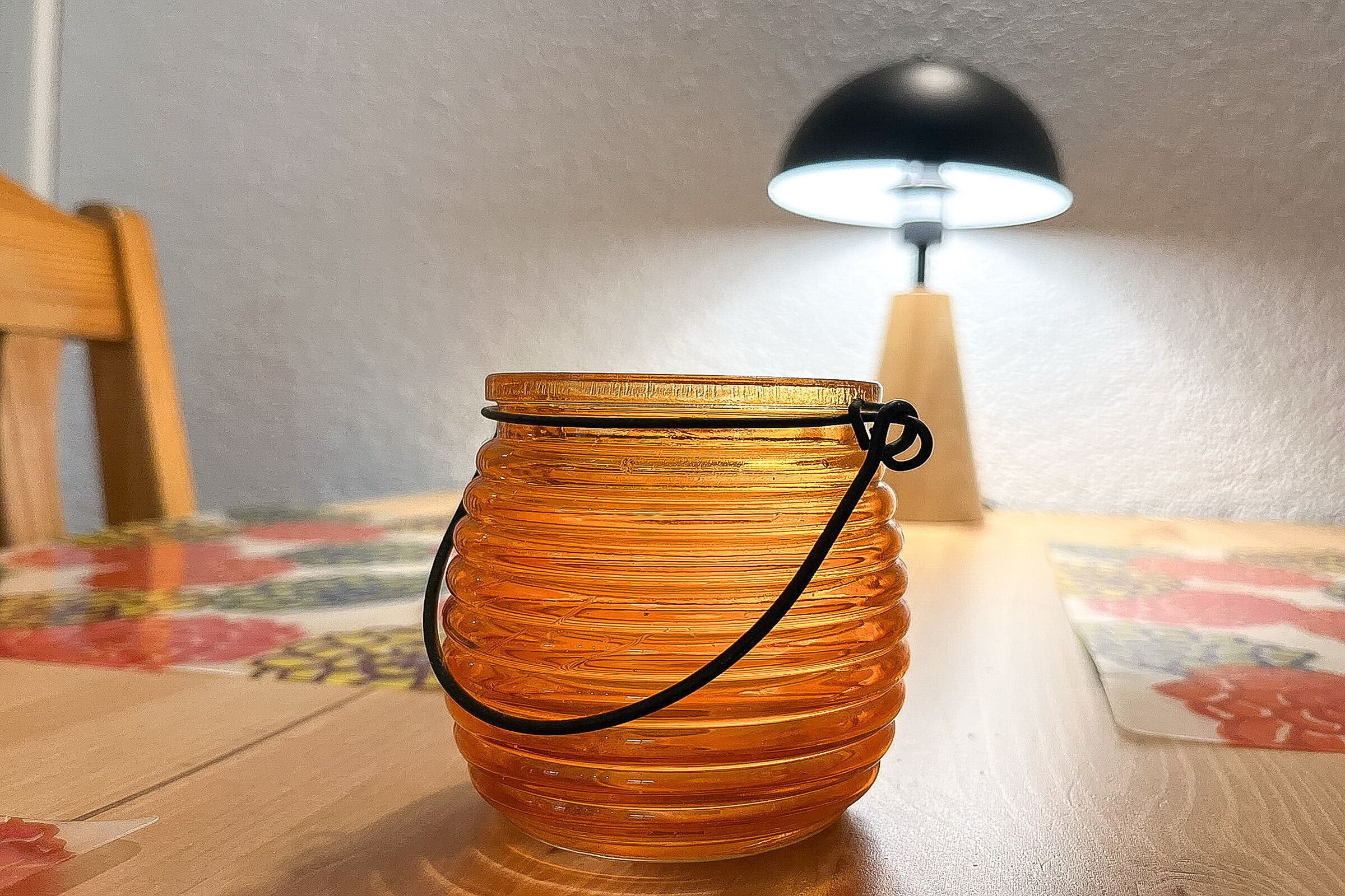 A glass jar with a black handle on a wooden table.