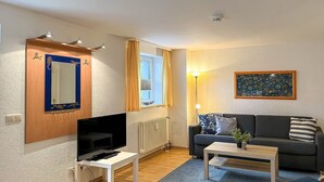 Ein Wohnzimmer mit Fernseher, Sofa, Couchtisch und einem Bild an der Wand.