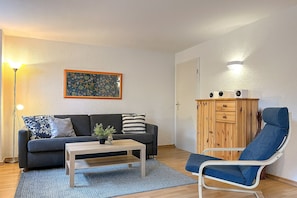 A living room with a sofa, coffee table, and a reclining chair. There is a wooden cabinet with drawers and a framed artwork on the wall. - Villa Triton Wohnung 07 (Ostseebad Boltenhagen)