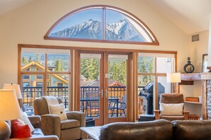 A room with a large sliding glass door leading to an outdoor deck, furnished with a sofa, chairs, and a table. - 3 Bedroom Penthouse  | Balcony + Fireplace (Canmore)