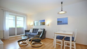 Un salon moderne comprenant un canapé, un fauteuil à bascule, une table à manger avec des chaises et une grande fenêtre avec des rideaux.