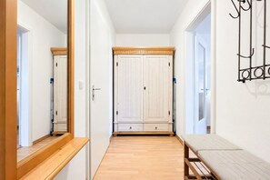A hallway with a wooden bench, a wardrobe with two doors, and a mirror on the left wall.
