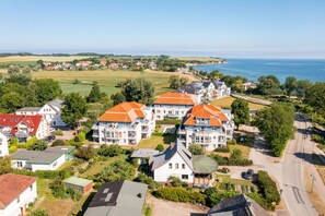 Ein Küstenwohngebiet mit Häusern, deren Dächer rot und die Wände weiß sind, umgeben von Grünflächen und freiem Blick auf das Meer.