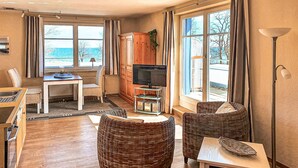 Een gezellige woonkamer met rieten meubels, een televisie en grote ramen met uitzicht op zee.