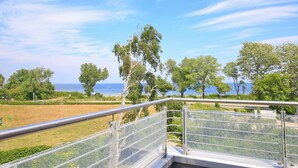 A balcony with a metal railing overlooking a coastal landscape with trees and a view of the sea. - Dünenblick Wohnung 50 (Ostseebad Boltenhagen)